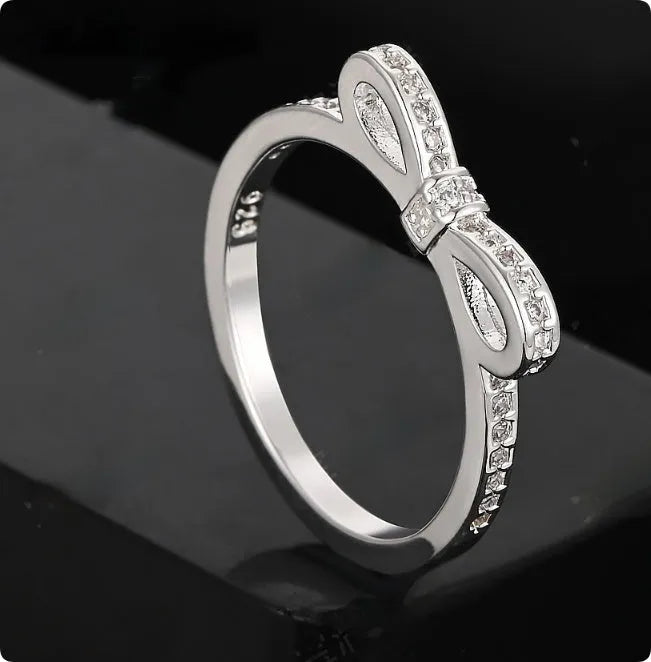 Silver coloured ring with a detailed three-dimensional bow design set with sparkling zircon crystals on a finger.