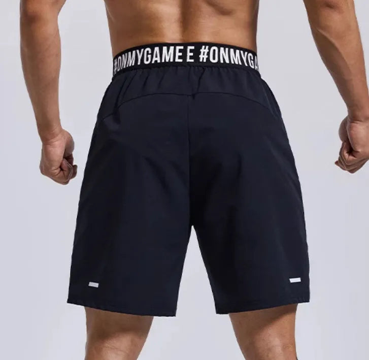 Man modelling black loose-fit cropped sports shorts with letter detail and an elastic waistband.