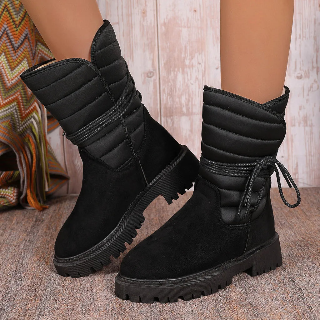 A pair of women's chunky heel snow boots in suede with a lace-up front and fleece lining, shown in black.