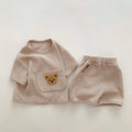 Unisex baby summer suit with bear print cotton top and beige shorts on a neutral background
