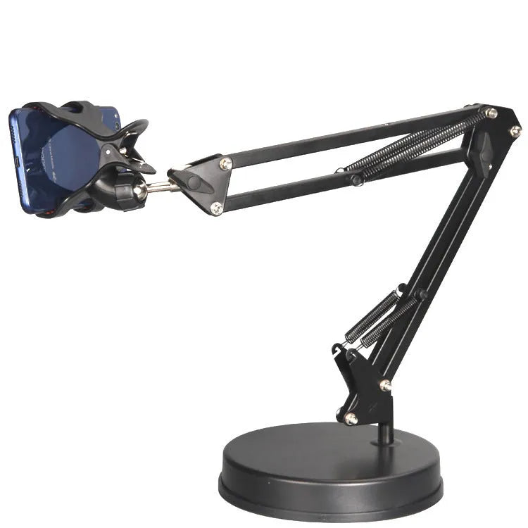 Black universal phone stand with long rotating metal arm and heavy circular base on a wooden desk.
