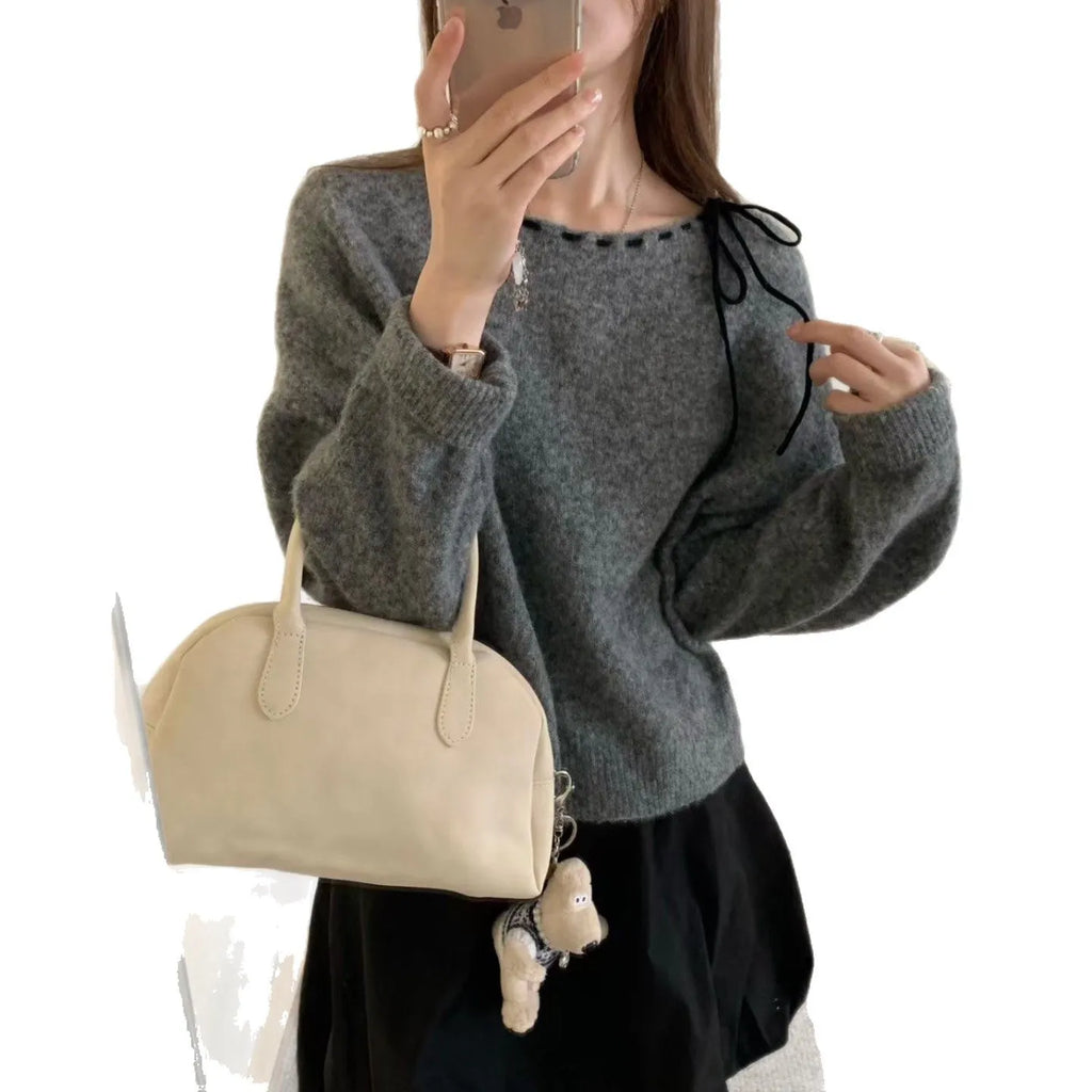 A grey women's loose-fitting knitwear pullover on a hanger, showing its casual style.