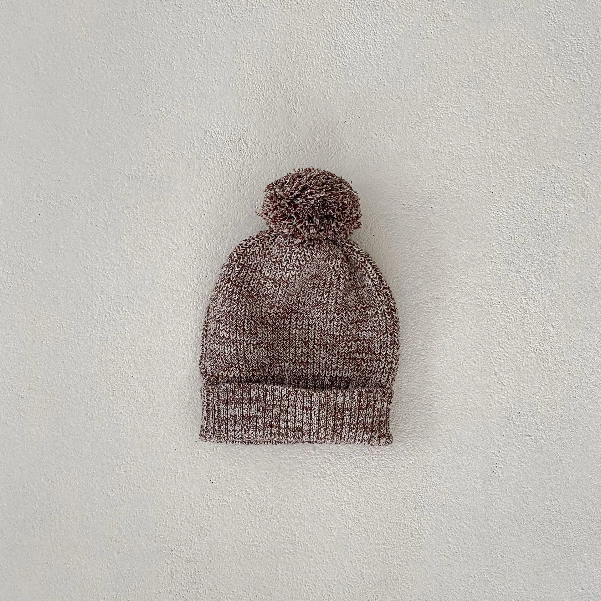 Dark brown knitted three-piece set for infant girl with fur ball hat, blouse, and shorts.
