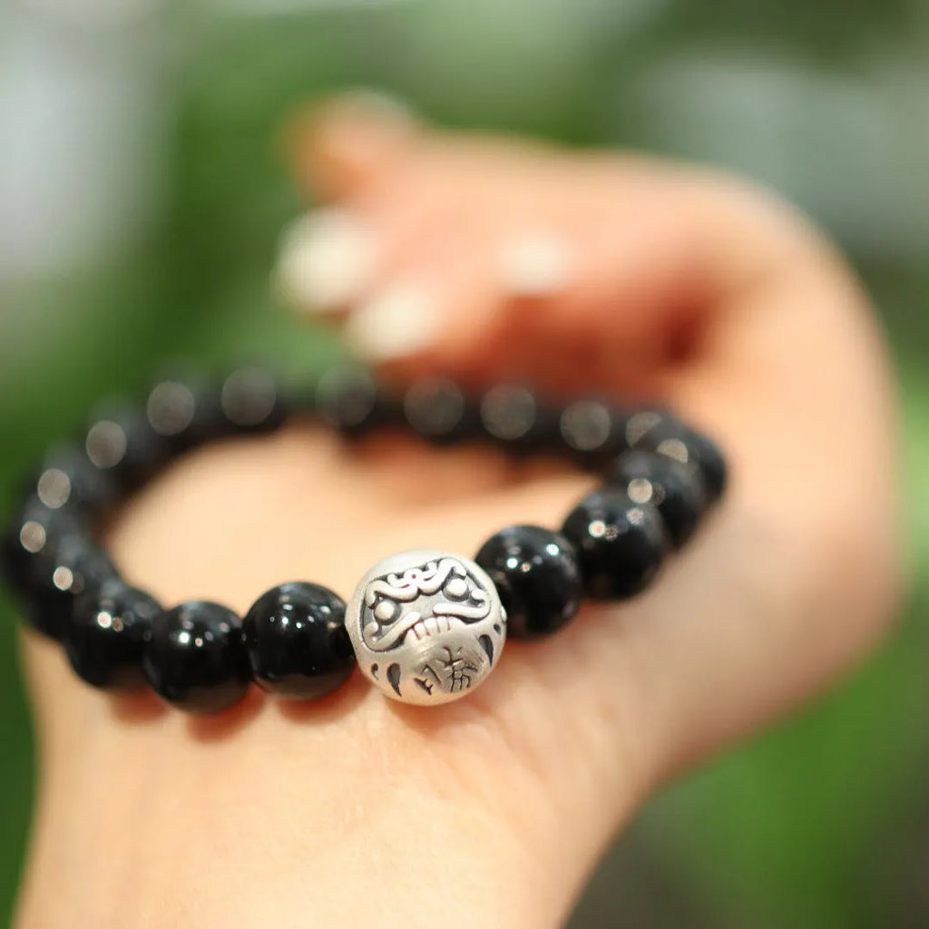 Close-up of a black bracelet with 10mm agate beads and sterling silver details on a wrist.