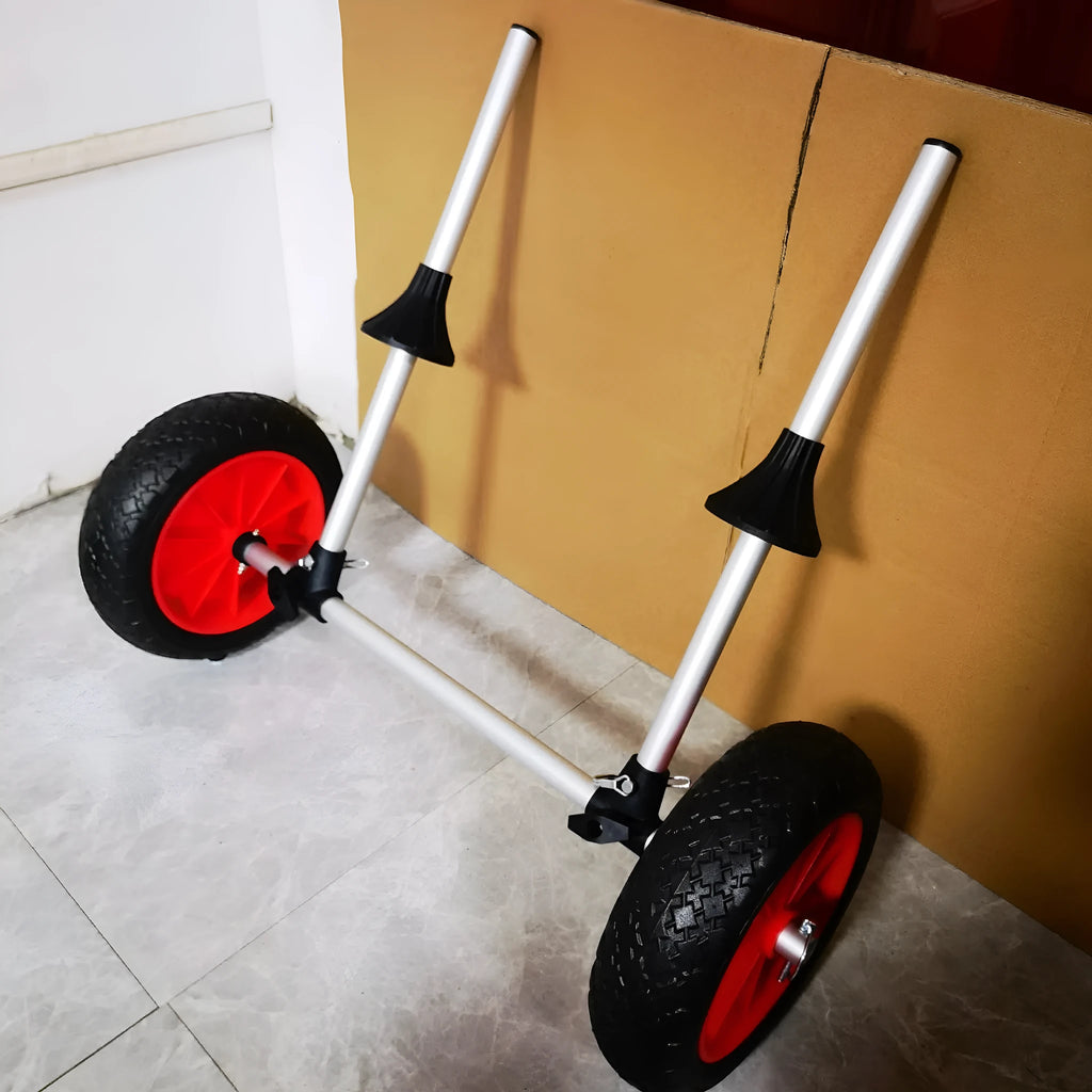 Foldable aluminium kayak handcart with large rubber wheels, shown carrying a yellow kayak on a beach.