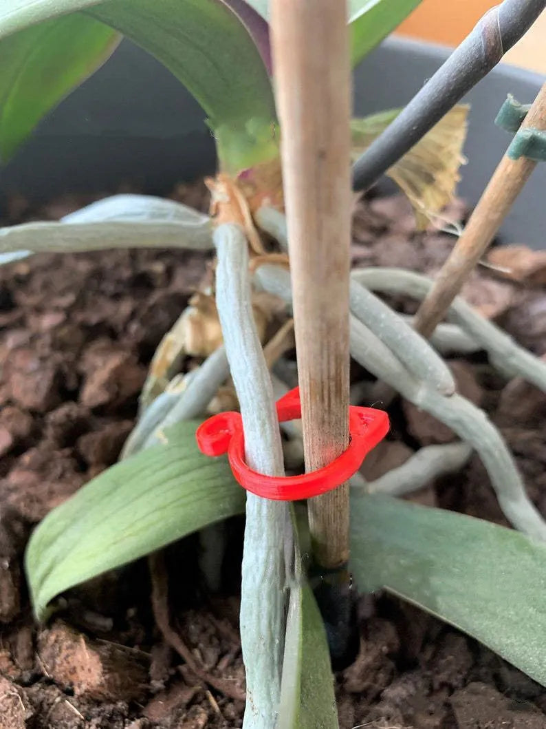 A small red cat-shaped plastic clip for holding plant stems, shown next to a green leaf.
