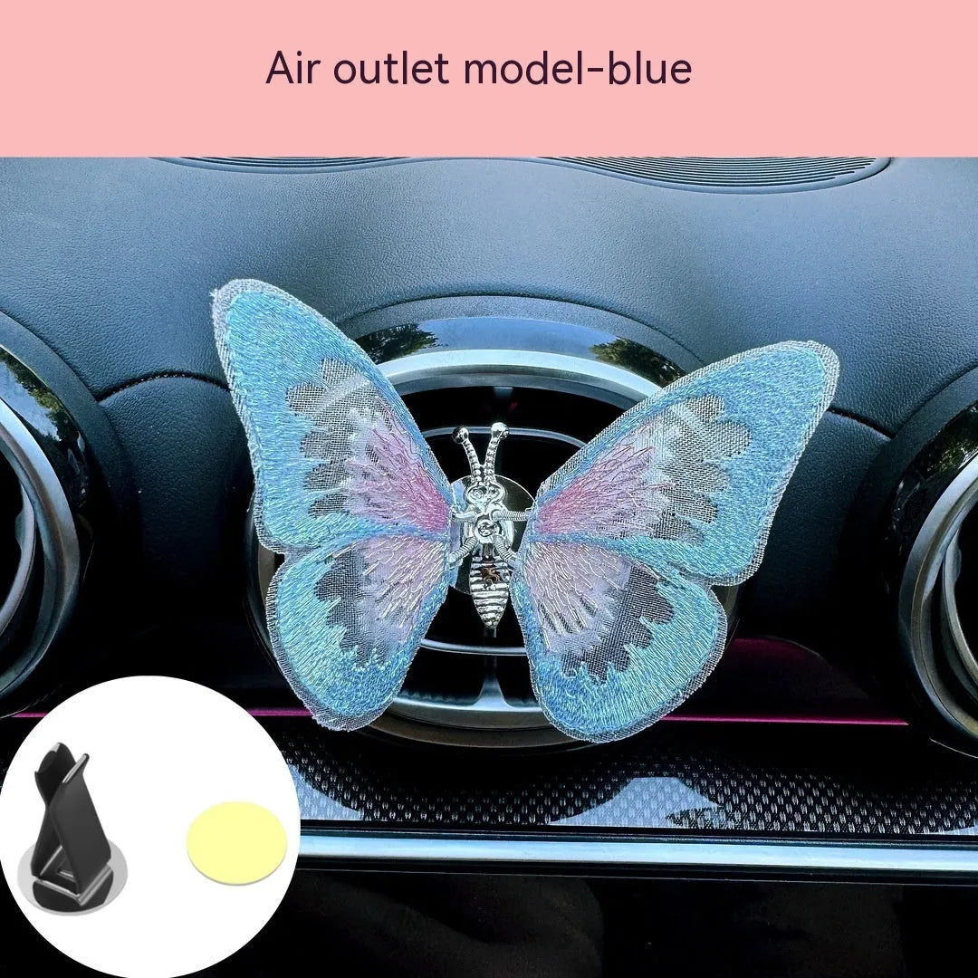 Soft fabric embroidered butterfly car air vent decoration in multiple colour options on a centre console.