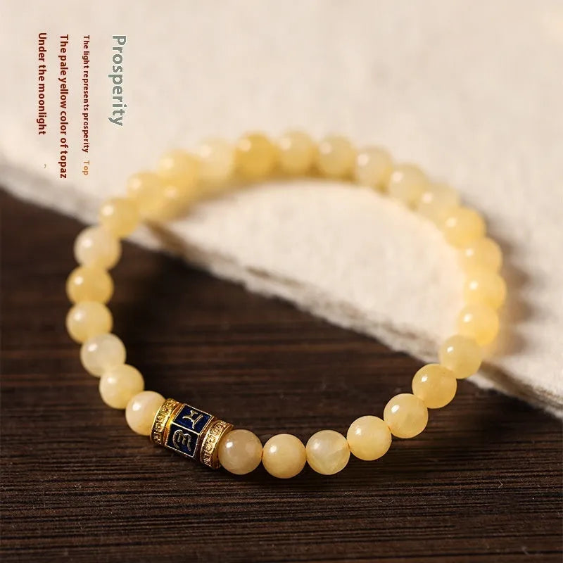 Close-up of a women's hand-woven bracelet with topaz-coloured barrel beads, square jade beads, and a fu charm.