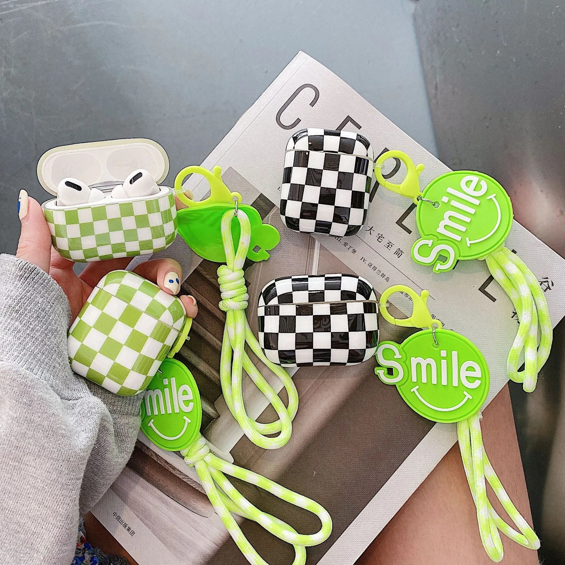 Black and green checkerboard pattern TPU protective case sleeves for Apple AirPods, one with a smiley face lanyard attached.