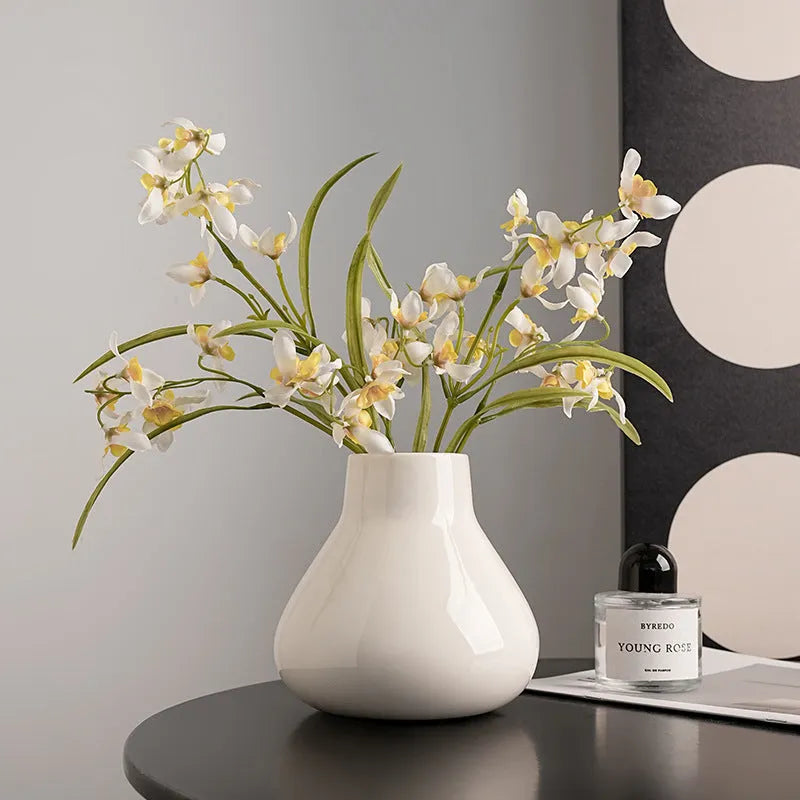 Black ceramic round belly French decorative vase with artificial flower stems on wooden surface