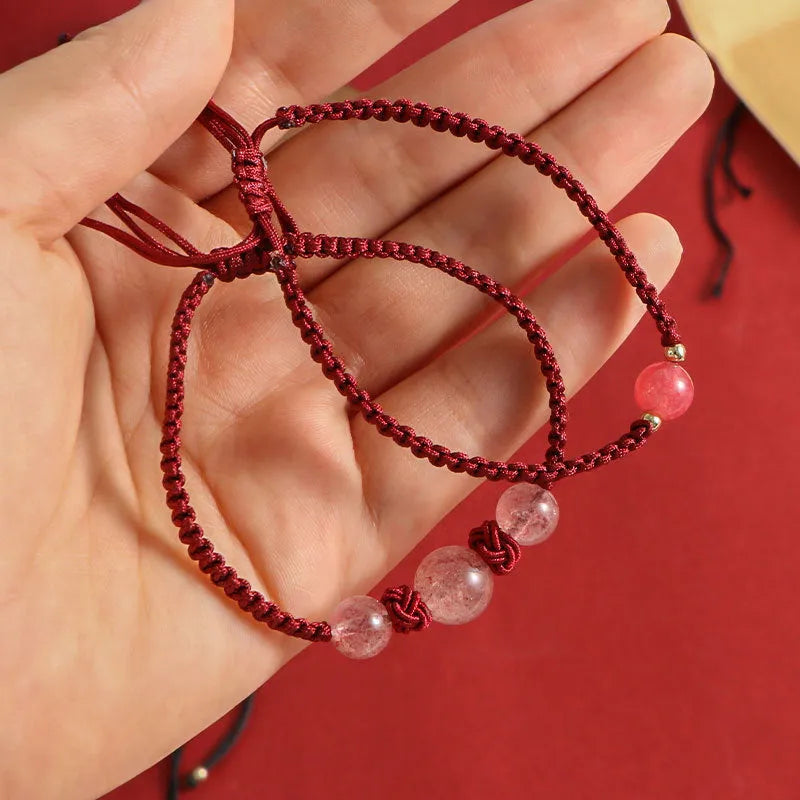 A woven red rope bracelet with a natural strawberry quartz bead and an alloy clasp.