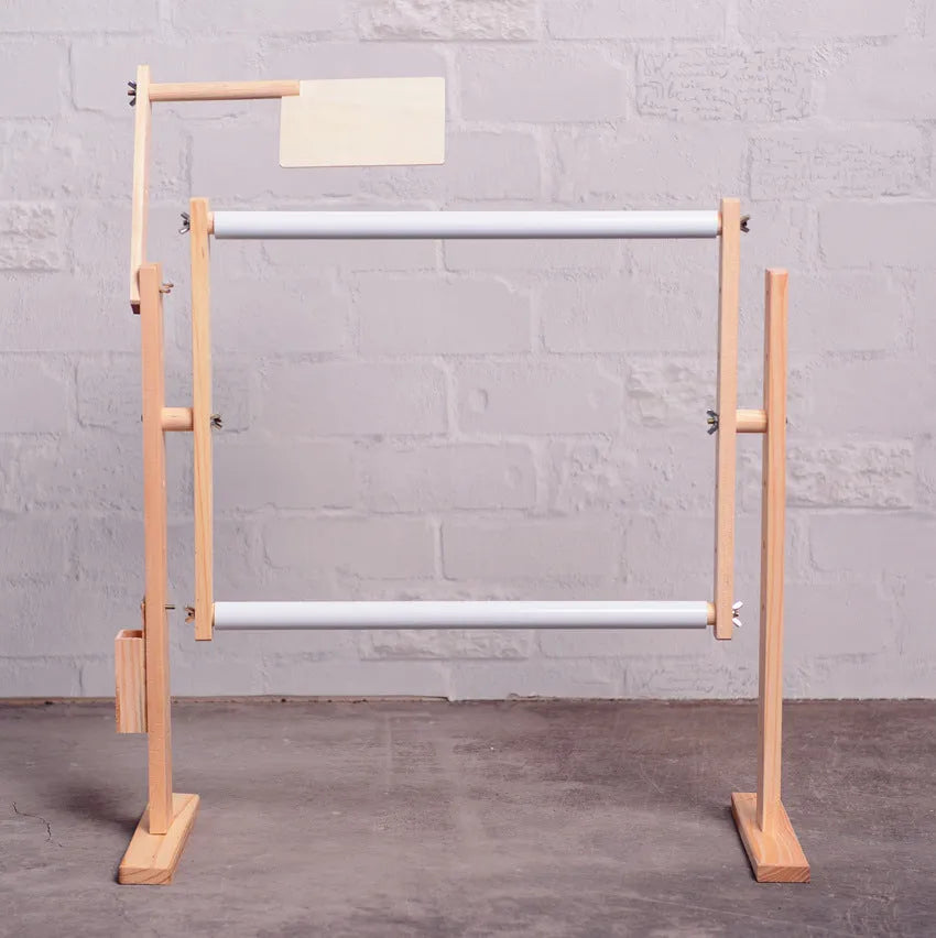 Vertical solid pine wood cross stitch embroidery frame with adjustable clamp on a desktop.