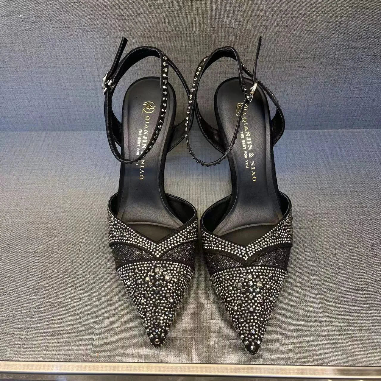 Women's black hollow high heel shoe with red sole and pointed toe, shown next to a silver pair.
