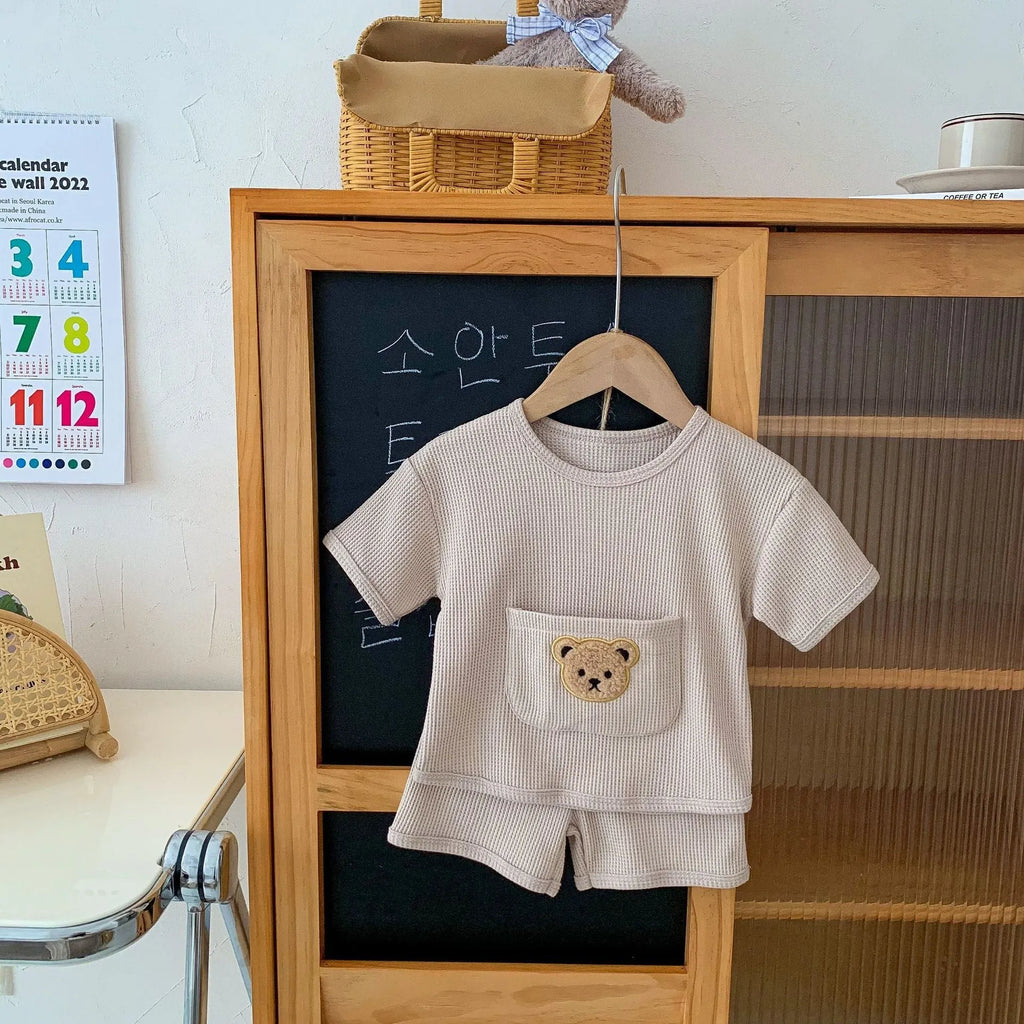 Unisex baby summer suit with bear print cotton top and beige shorts on a neutral background