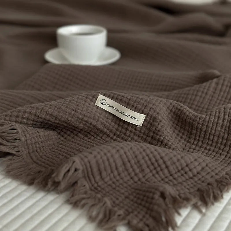 Cotton four-layer gauze blanket with tassel trim in avocado green colour, laid flat.