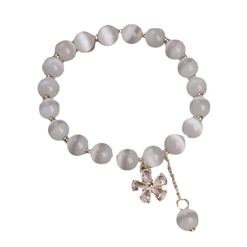Women's white cat's eye stone bracelet with floral detail and a safety buckle pendant on a single loop.