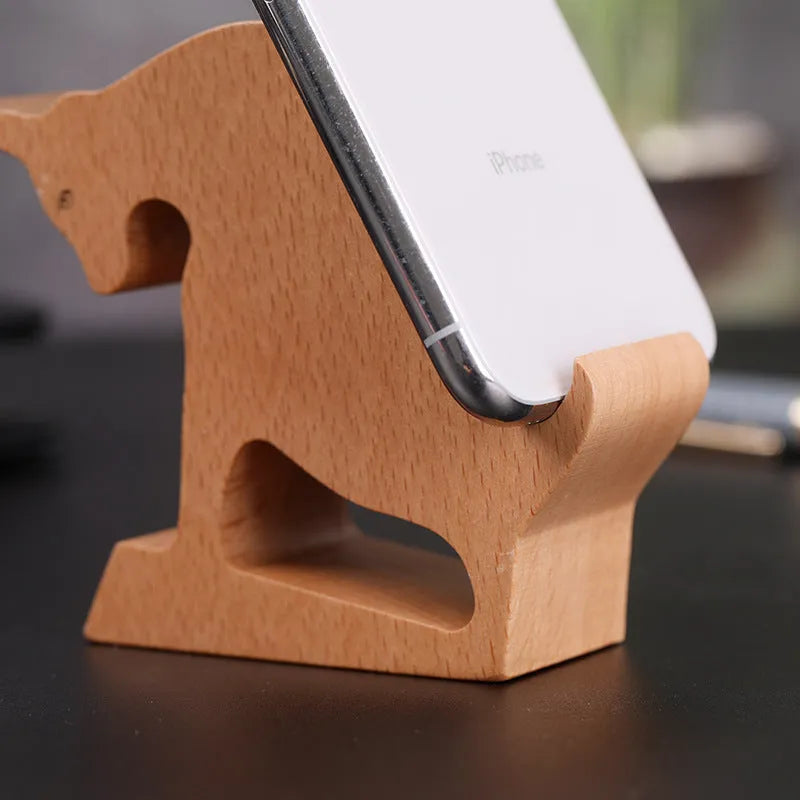 Solid beech wood phone stand with a decorative resin puppy figurine, holding a mobile phone at an angle with a charging cable threaded through the back.