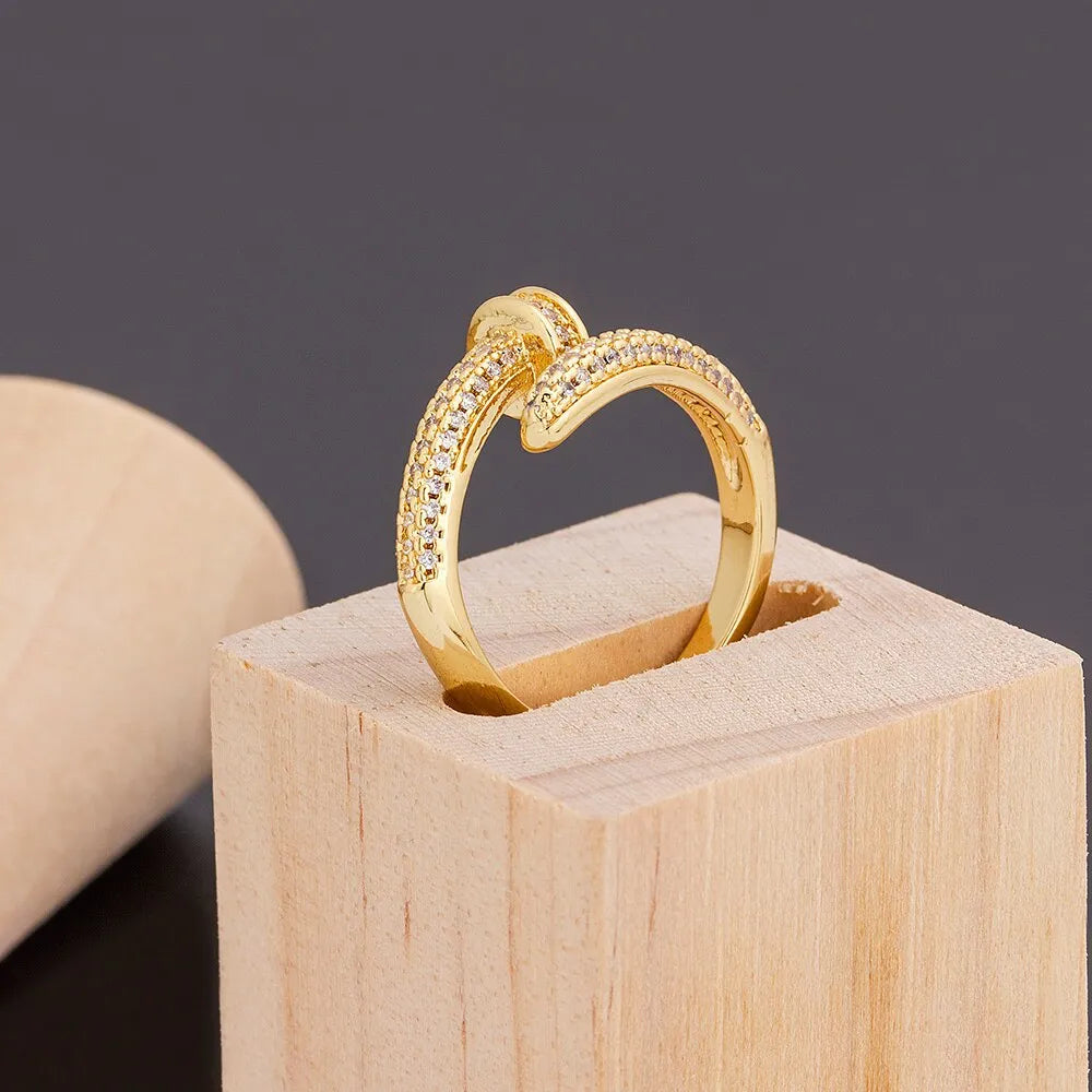 Close-up of a gold plated geometric nail ring with inlaid drill details on a metallic surface.