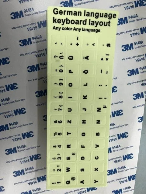 Glowing yellow multilingual keyboard stickers showing Arabic, Thai, Hebrew, French, Italian and German characters