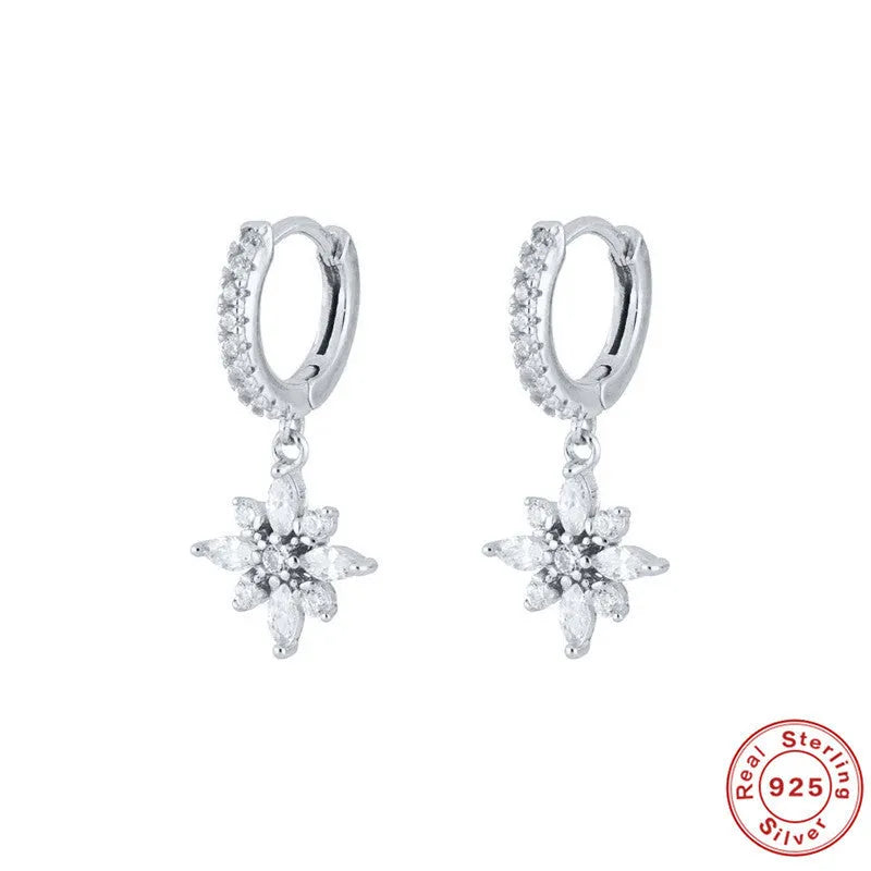 A pair of sterling silver snowflake pendant earrings with a gemstone, shown in yellow gold and white gold colour finishes.