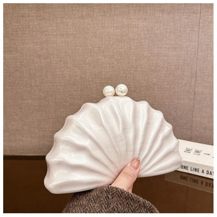 Acrylic shell-shaped clutch bag in champagne with silver chain on white background