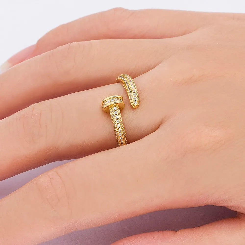 Close-up of a gold plated geometric nail ring with inlaid drill details on a metallic surface.
