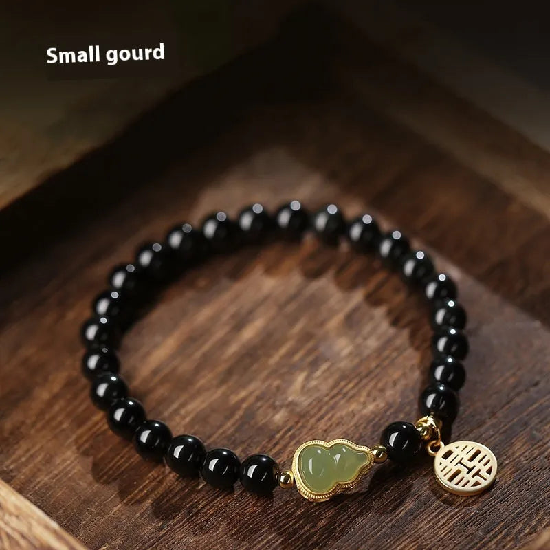 Black obsidian bracelet with a carved Hetian jade gourd charm, showing geometric beads.