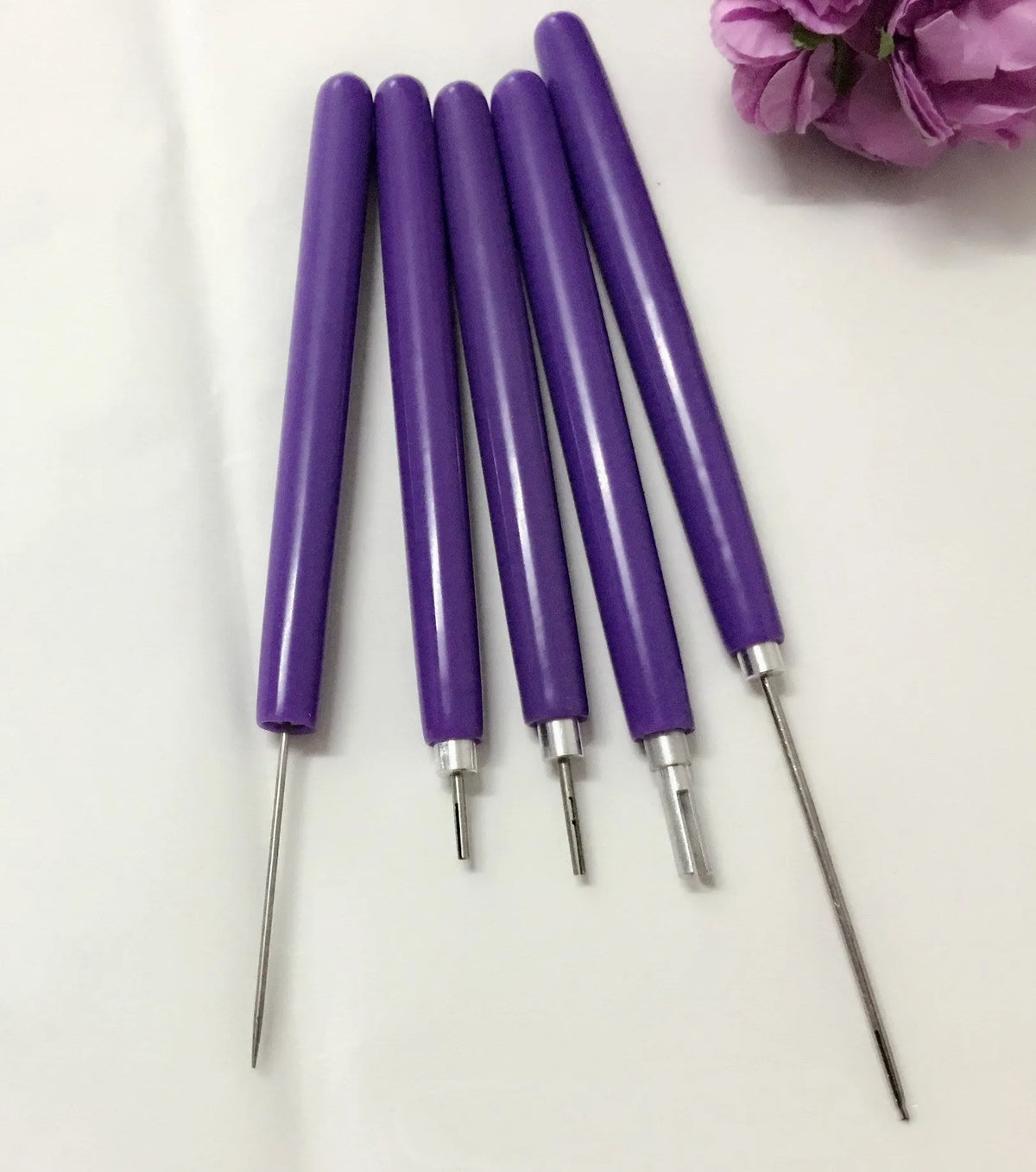 Purple quilling paper tool set with five slotted pens and needle stylus on white background