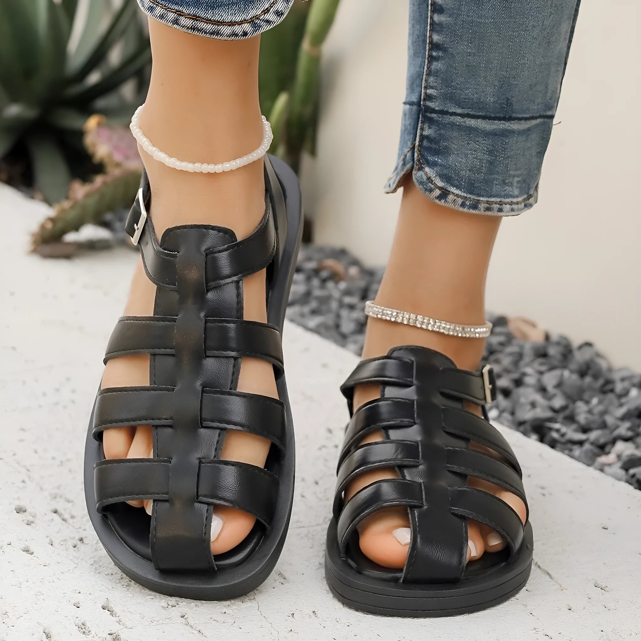 Flat Roman style women's sandals with buckle, black PU upper and rubber sole, side view
