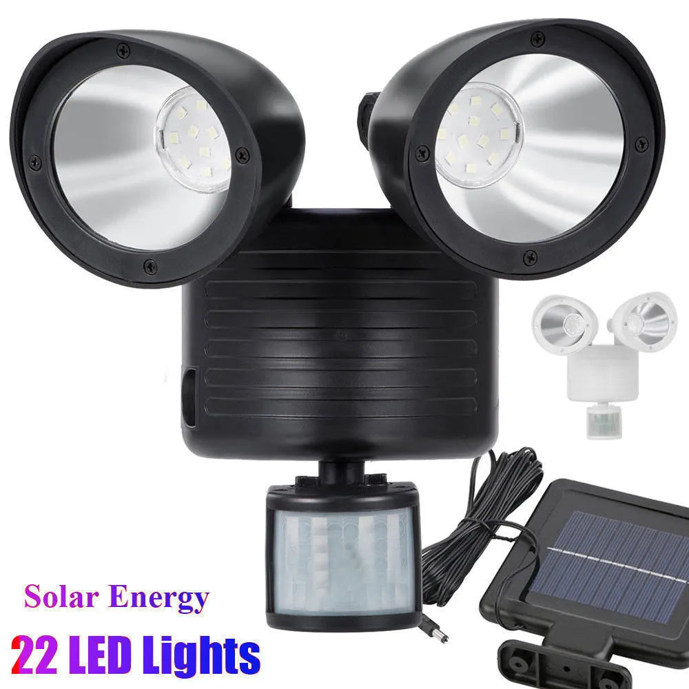 Black dual-head solar security spotlight with solar panel on top mounted on an outdoor wall.