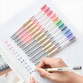 Pack of twelve black Muji gel pens with 0.5mm nibs, caps removed, on a notepad.