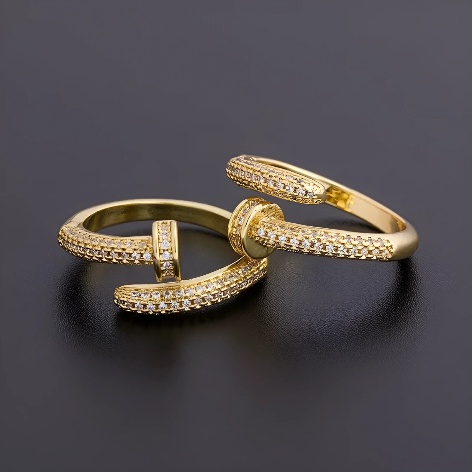 Close-up of a gold plated geometric nail ring with inlaid drill details on a metallic surface.