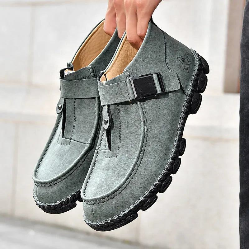 Men's black synthetic leather slip-on shoes with visible handmade stitching and a flat sole