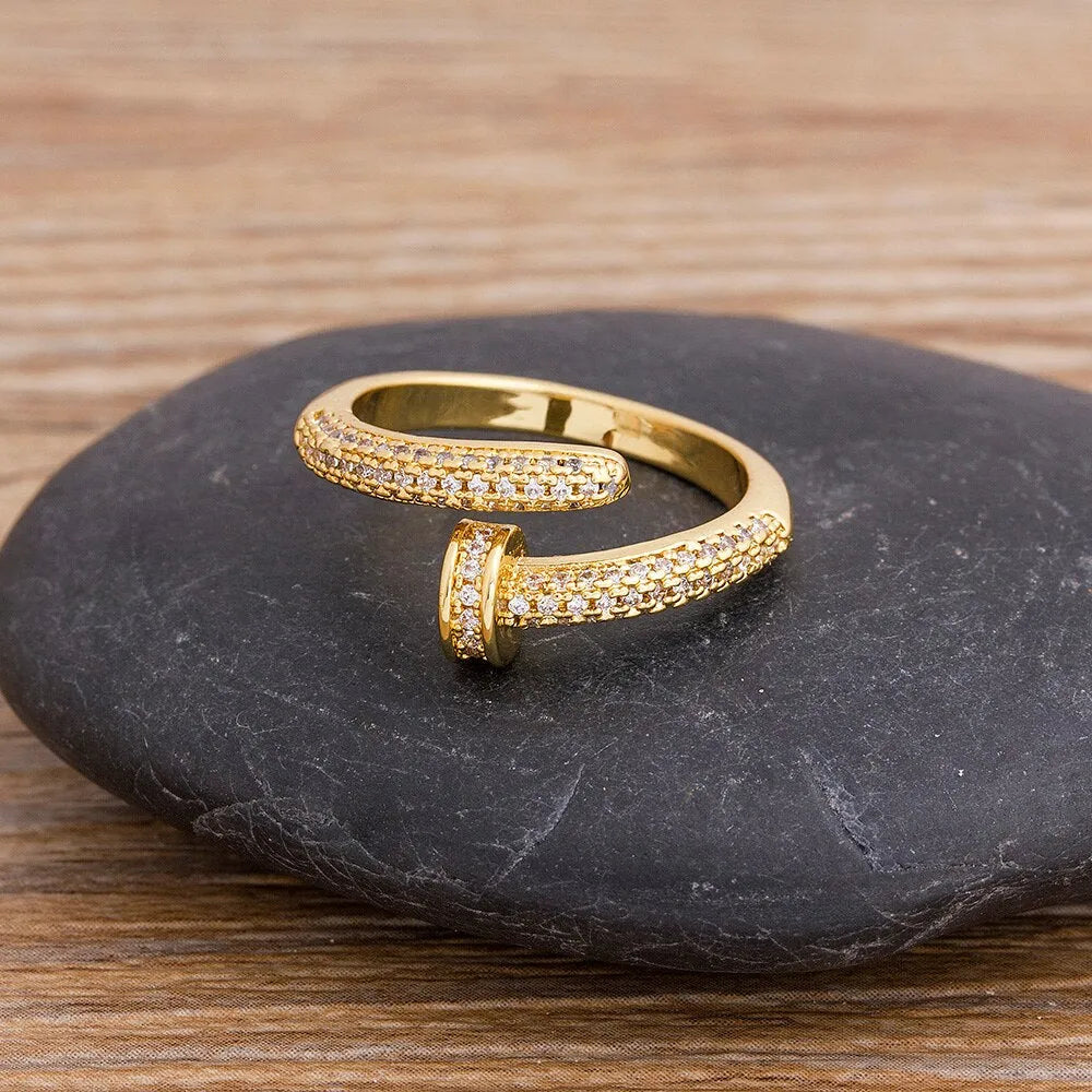 Close-up of a gold plated geometric nail ring with inlaid drill details on a metallic surface.