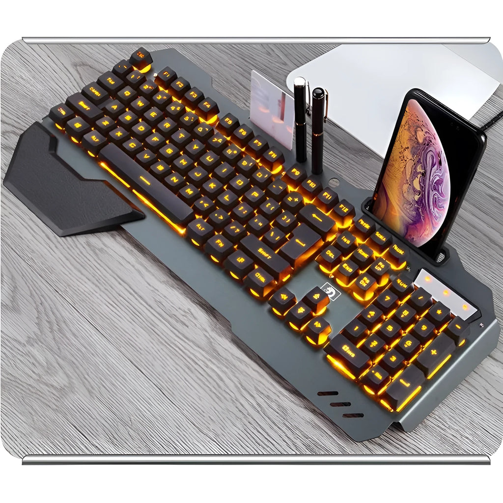 Black wired gaming keyboard with RGB backlight, phone holder, pen tray, and magnetic wrist rest on a desk