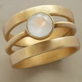 Gold-plated geometric titanium steel ring with a micro-inlaid white chalcedony stone on a grey background.