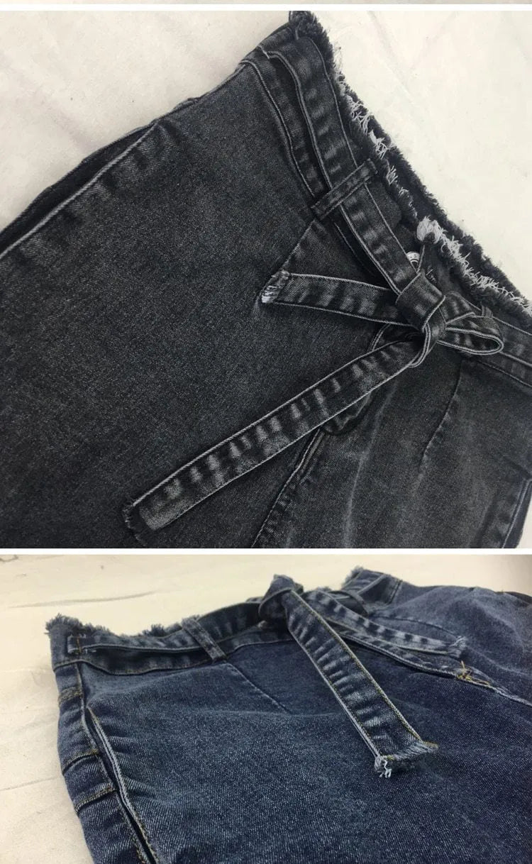 Pair of light blue fringed jeans with distressed hem detailing on a denim background.