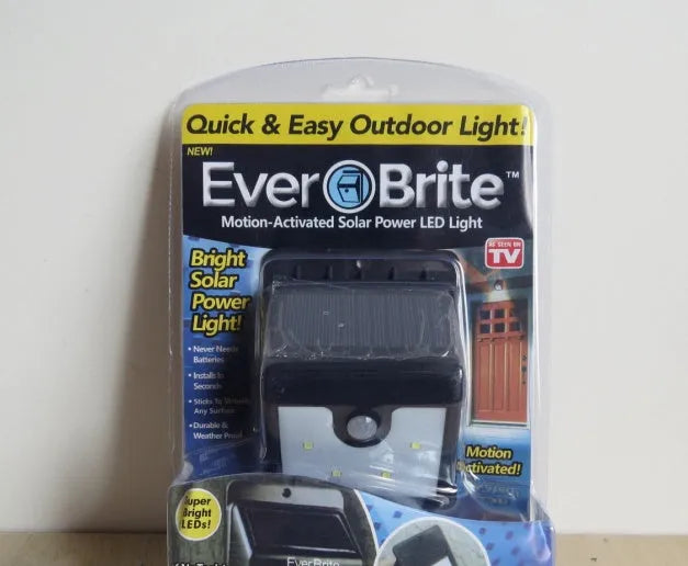 White round solar-powered motion sensor light on an adjustable metal stake in a garden setting.