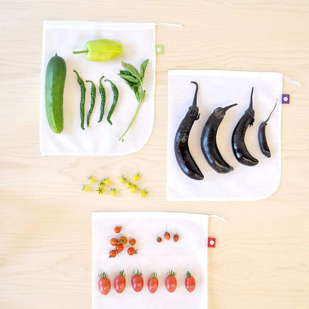 Five white cotton drawstring bags for kitchen vegetable storage arranged on a clean surface