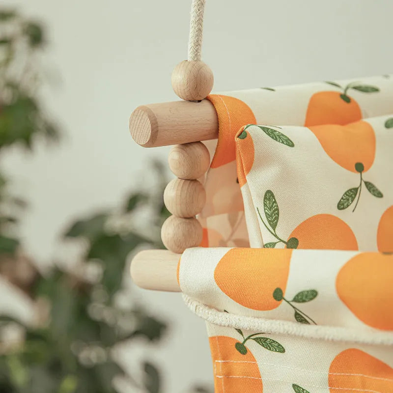 Cotton canvas baby swing chair with wooden seat and colourful tassel, hanging indoors.
