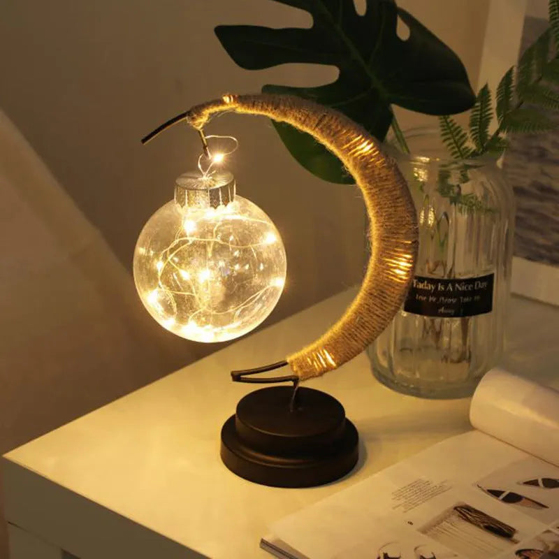 Moon ball shape LED night light with crescent holder, PVC shell, warm light on a wooden table