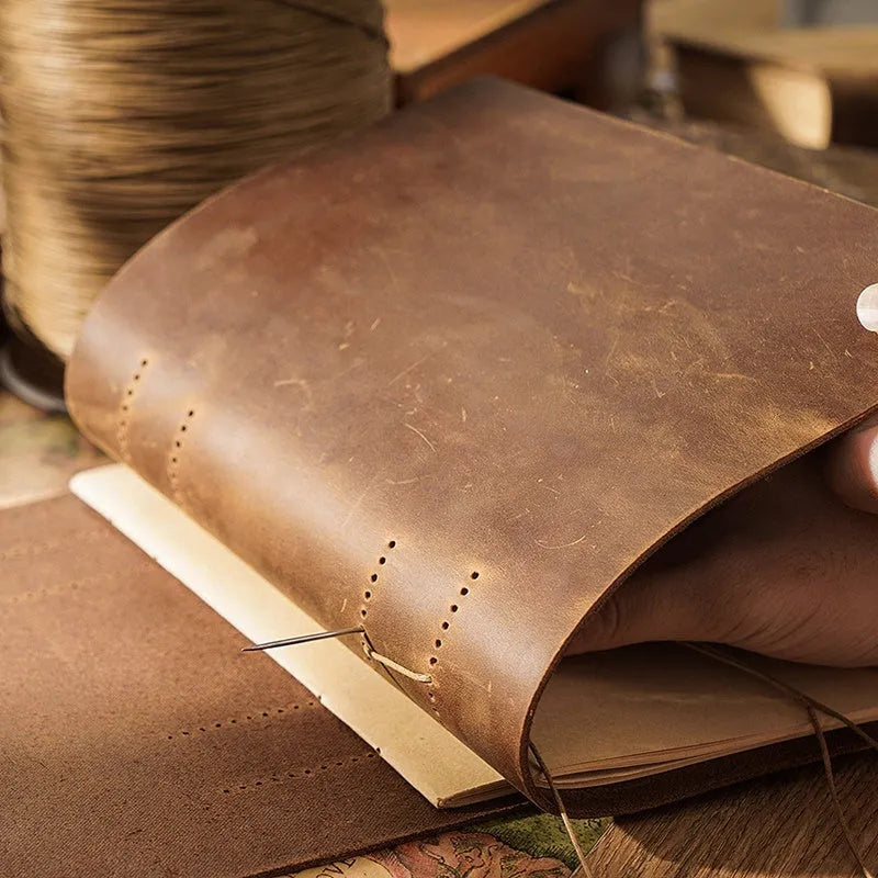 Brown handmade cowhide leather notebook with 200 pages, 19x14cm paper size, lying open on a wooden desk
