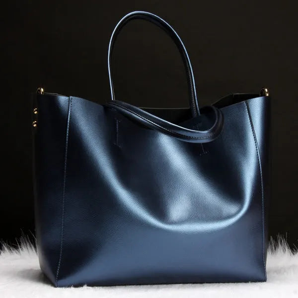 Women's cowhide leather shoulder bag in black with adjustable strap shown next to a silver version.