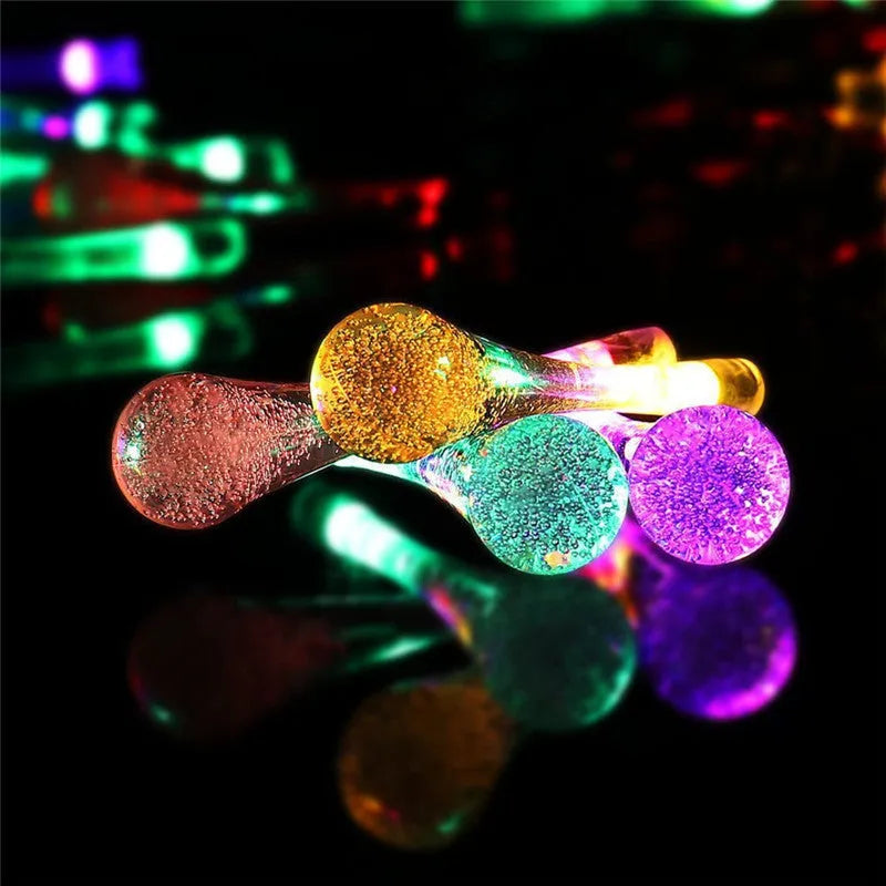 6.5 metre long solar-powered outdoor string lights with water drop shaped pendants on a green lawn.