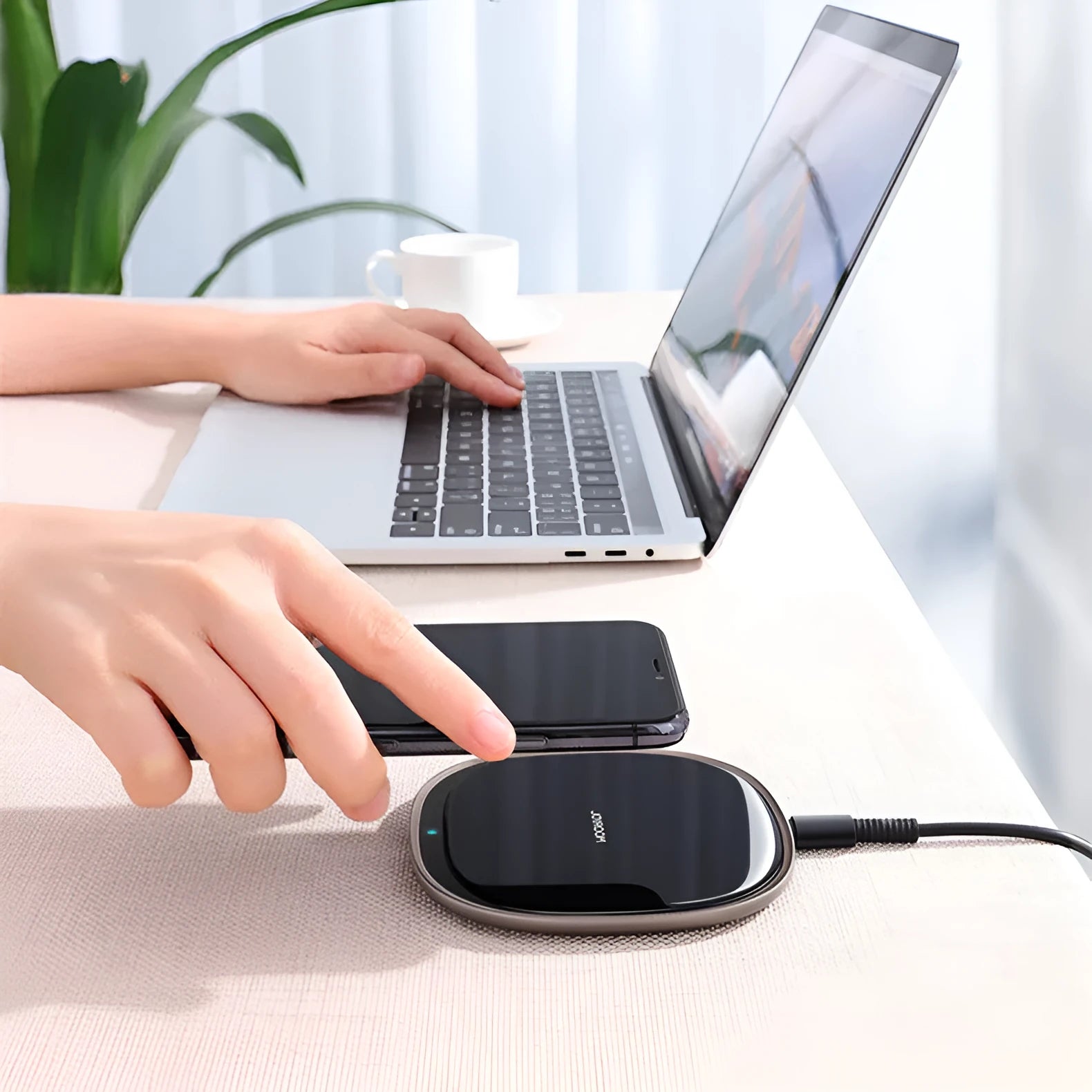 Black square 15W Qi wireless charging pad on a wooden desk next to a mobile phone.