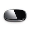 Black square 15W Qi wireless charging pad on a wooden desk next to a mobile phone.
