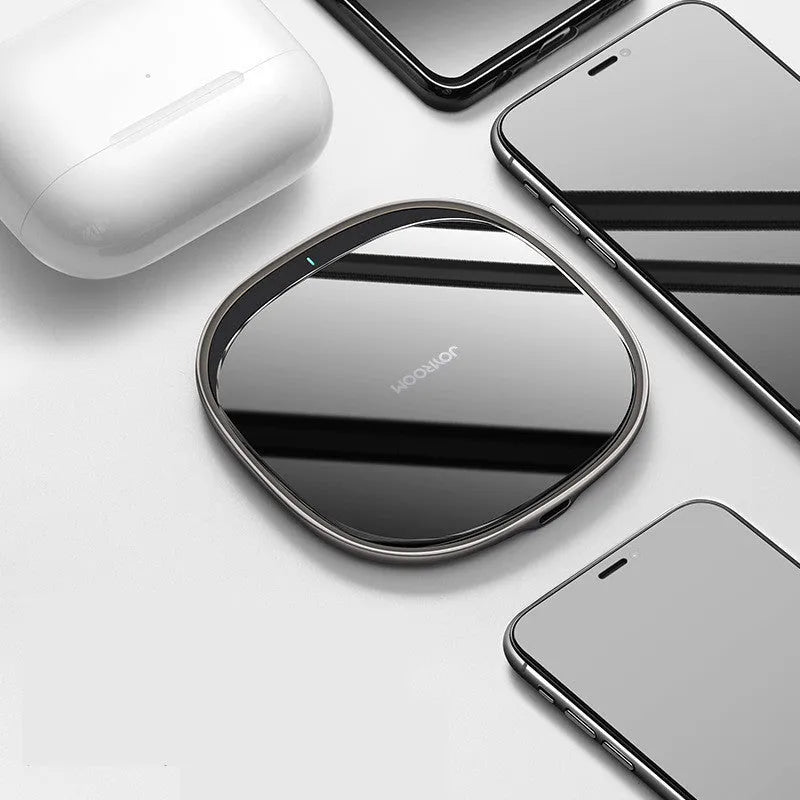 Black square 15W Qi wireless charging pad on a wooden desk next to a mobile phone.