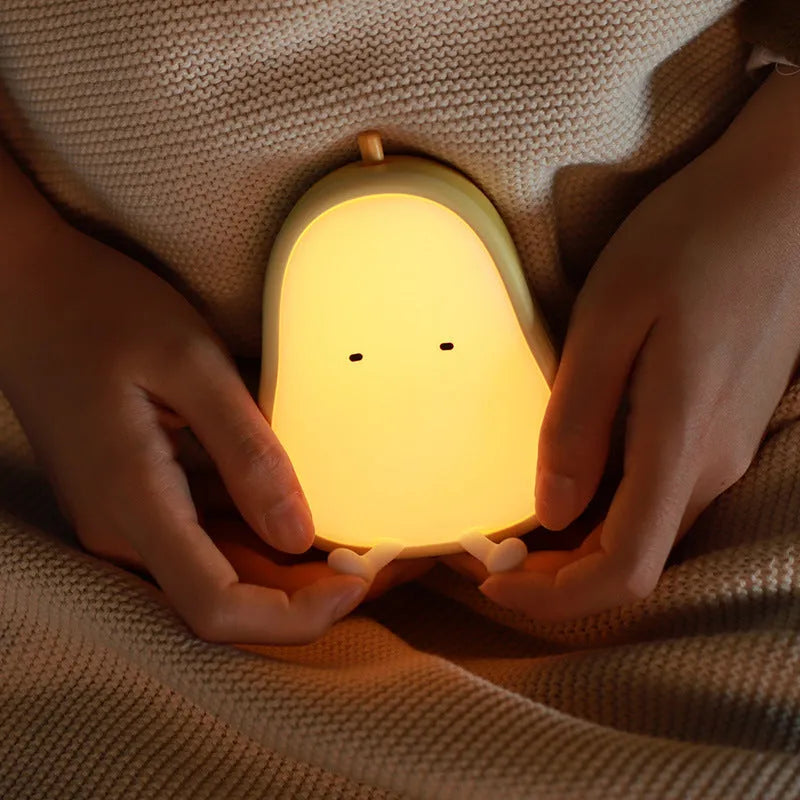 White silicone pear-shaped bedside night light emitting a warm yellow glow on a wooden table.