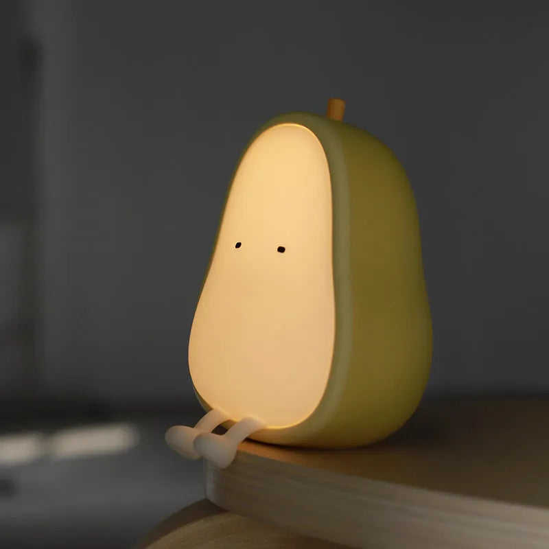 White silicone pear-shaped bedside night light emitting a warm yellow glow on a wooden table.