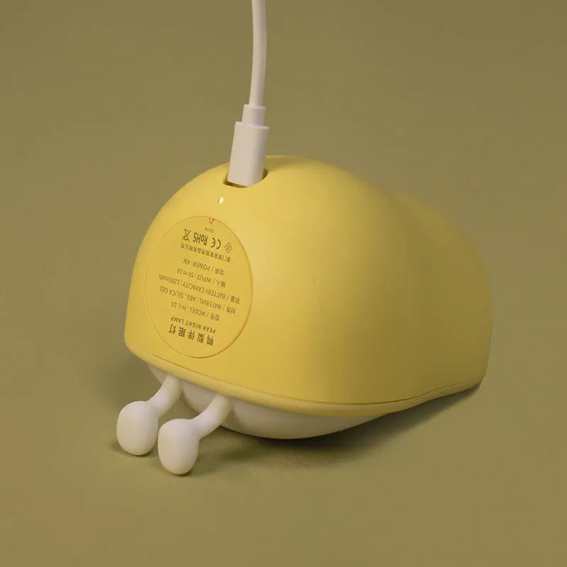 White silicone pear-shaped bedside night light emitting a warm yellow glow on a wooden table.